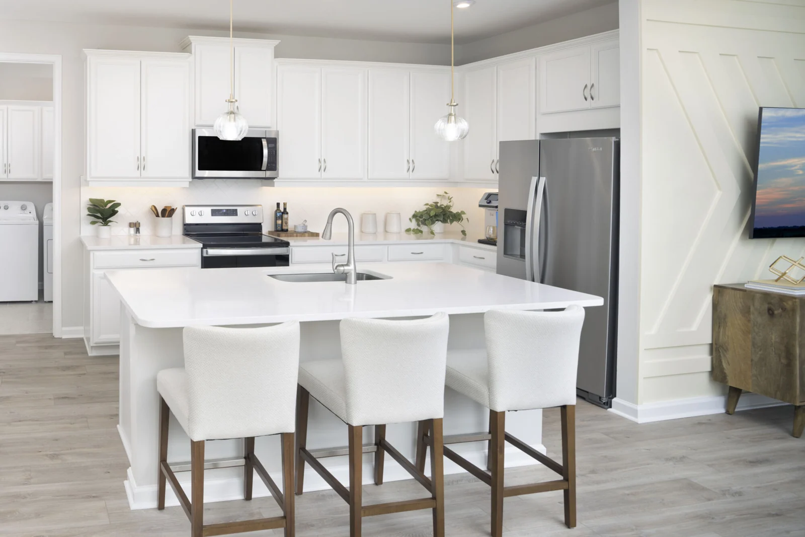 L-Shaped Kitchen with range, refrigerator, white cabinets, washer-dryer, pendant light and wood flooring