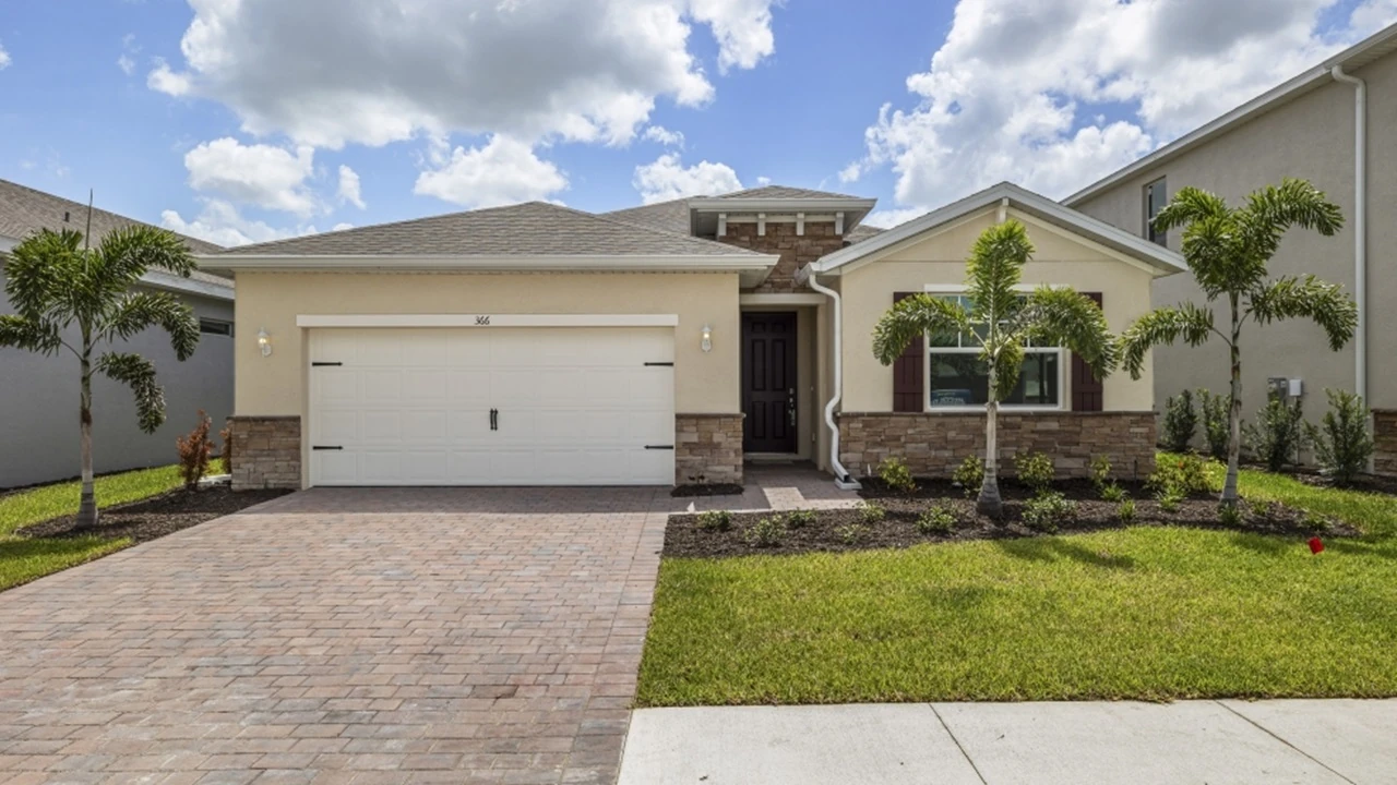 Outside of the Delray model. Yellow home with two car garage, one window with shutters, and front door. Mixed paver driveway.
